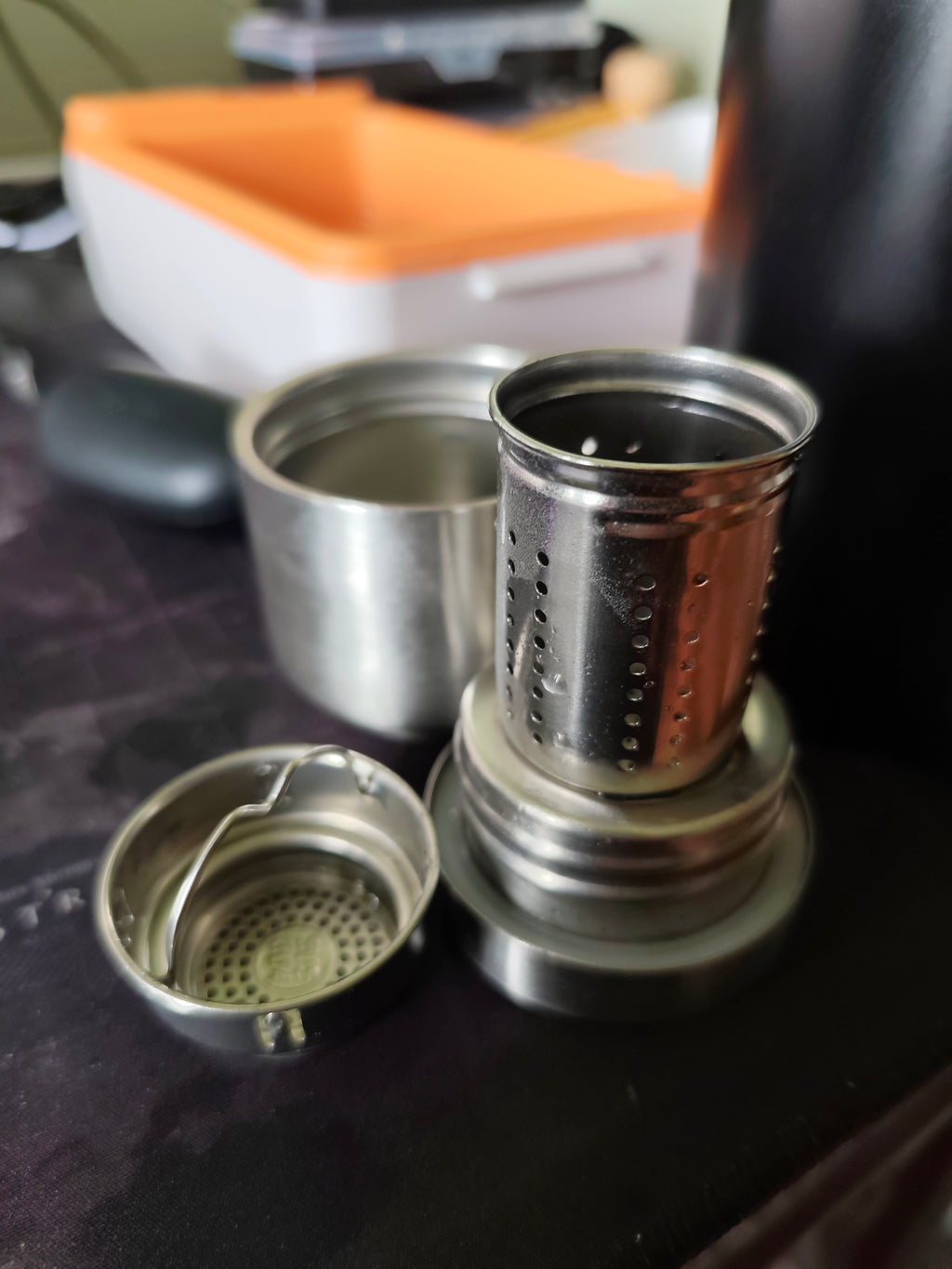 Real-life photo of the black 1200ml thermos sample opened, showing the removable perforated tea-leaf insert and stainless-steel cup