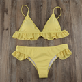 Yellow bikini top and matching bottoms laid flat on wood with under-bust ruffles and side frills